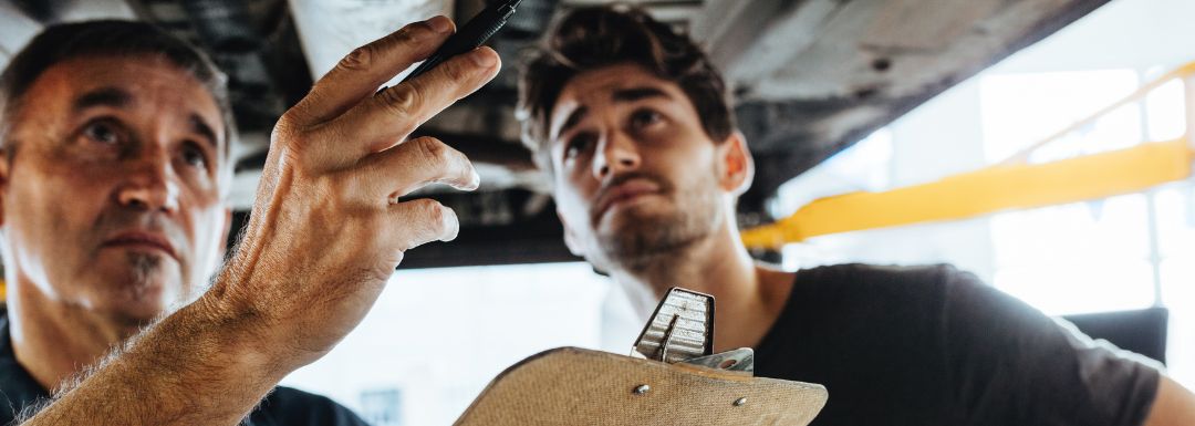 Technician inspecting a vehicle's undercarriage for maintenance issues.